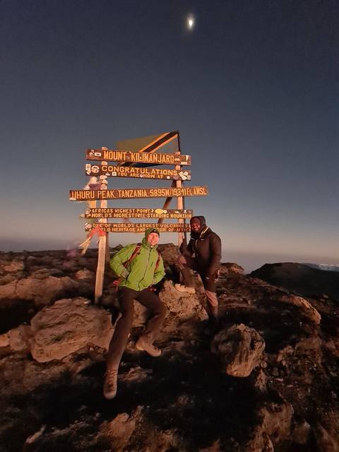 Two people next to the summit sign of Mount Kilimanjaro.