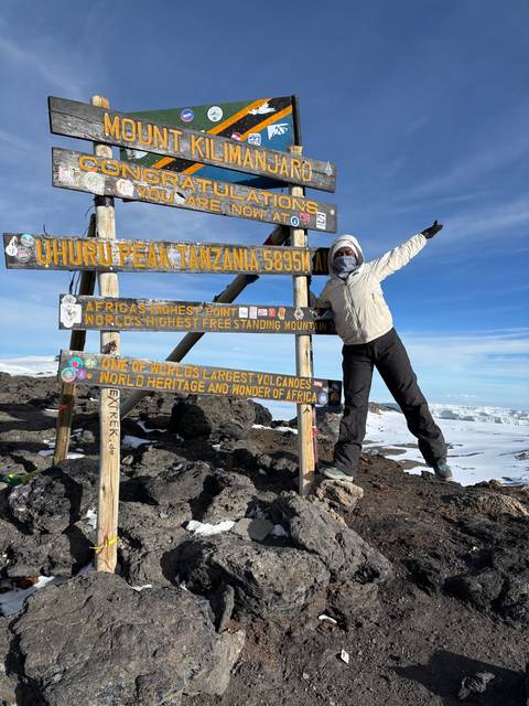       Person posing with a summit sign on Mount Kilimanjaro.
  
