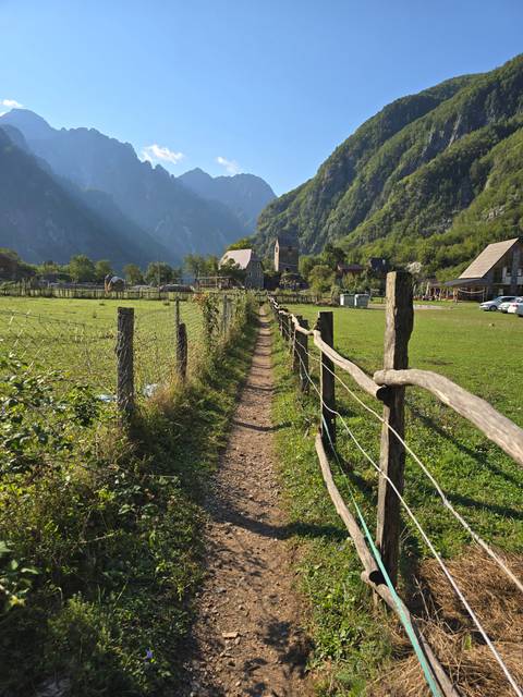       A dirt path lined with a wooden fence leading towards mountains.
  