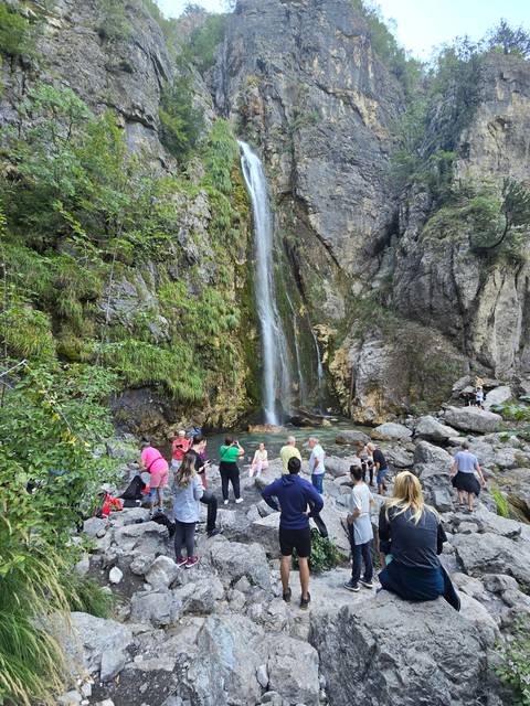 Group of people hiking toward a waterfall in a rocky area.