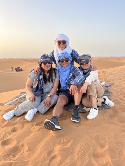       Group of people sitting on the sand in the desert wearing headscarves.
  