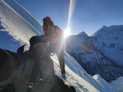 Climbers on a snowy mountain with a bright sun in view.