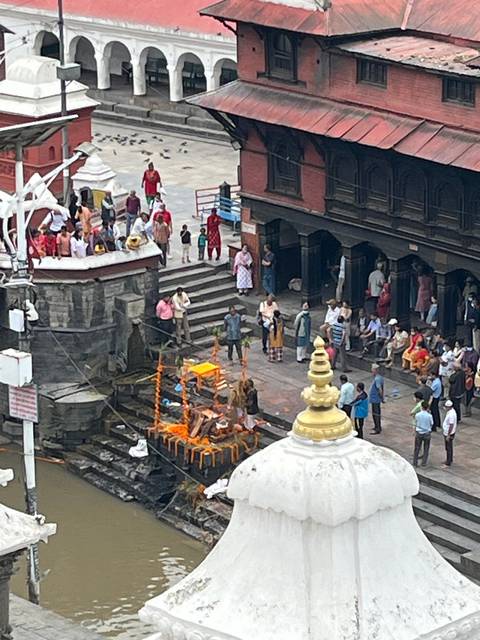       People gathering by a temple along a river with steps.
  