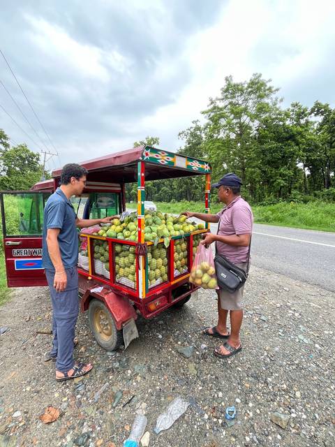       Two people at a fruit stand with a cart full of fruits.
  
