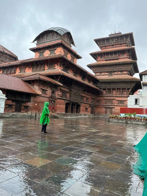 Person in a green raincoat near an ancient building.