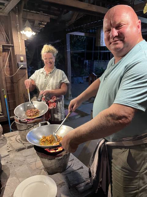 Two people cooking at an outdoor stovetop in an evening setting.