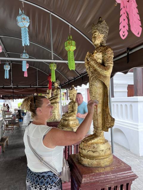 A person placing gold leaf on Buddha statues under a tent.