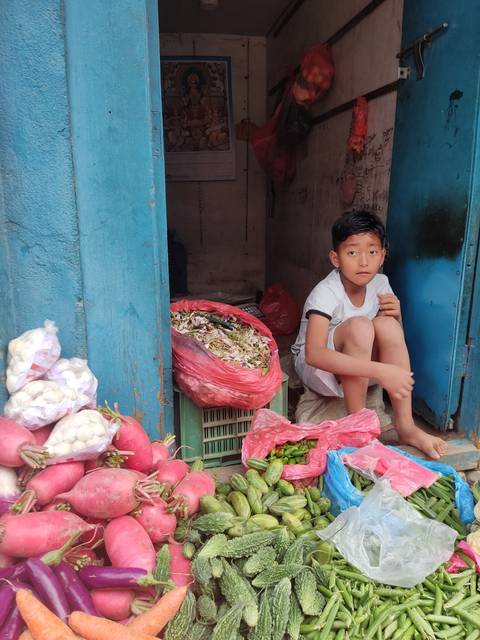       Child sitting in a vegetable market with fresh produce.
  