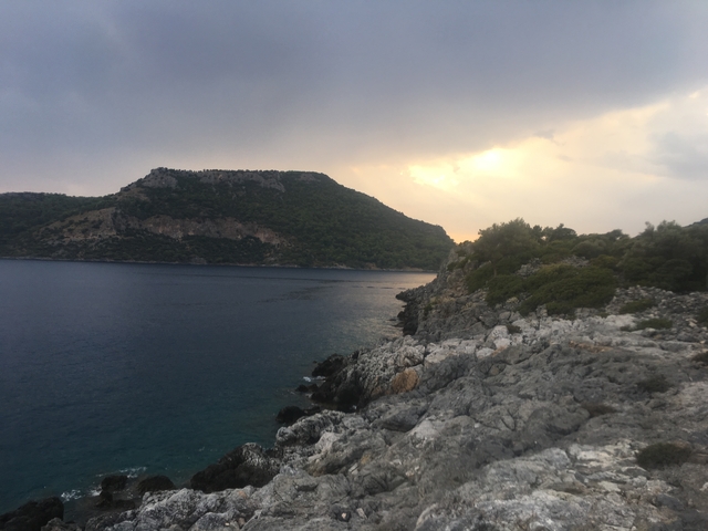 Cliffside view of the ocean with sunset in the distance.