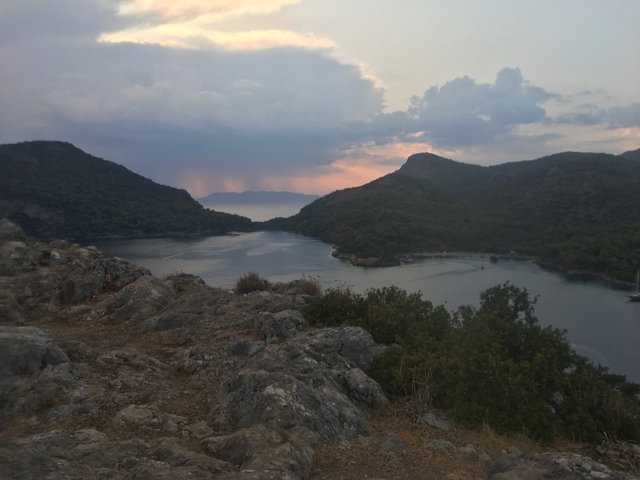       Sea view with two inlets surrounded by hills at sunset.
  