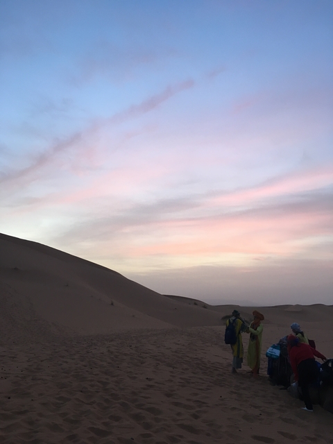 Sunset over desert dunes with pink sky.