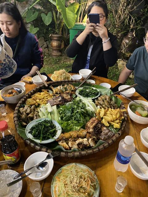       People sitting around a table with a large spread of food, including grilled meats and vegetables.
  