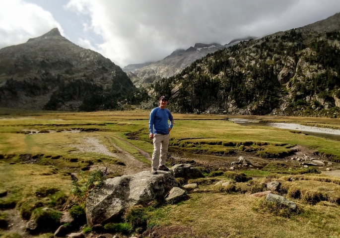 A man posing in an expansive mountain valley.
