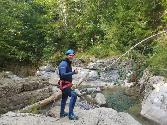       A person in outdoor gear giving a thumbs up near a stream.
  