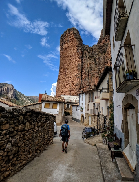 A person walking through a small European village surrounded by tall rocks.