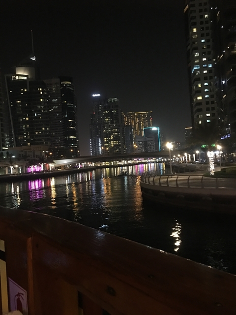 A view of a modern cityscape with lit buildings reflecting on water at night.
