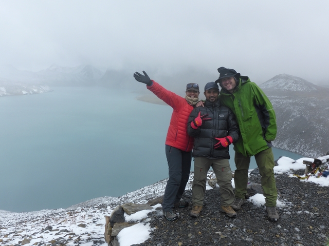 Three people posing by a lake in a mountainous area.
