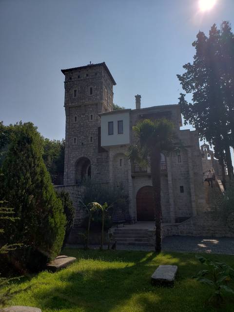 Stone castle with a tower in a lush garden setting.