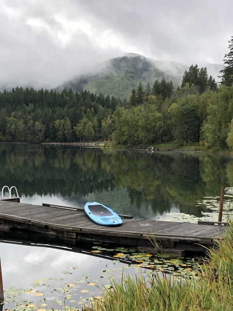 Calm lake reflecting surrounding trees with a paddleboard on the dock.