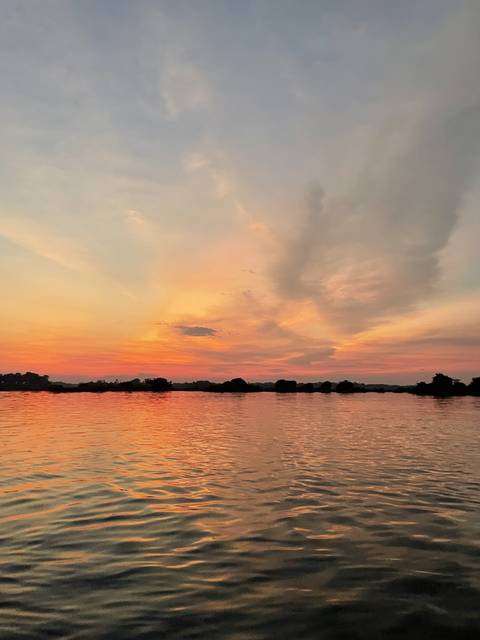       A colorful sunset over a body of water with dark silhouettes.
  