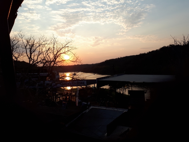       Sunset over a river with silhouetted structures.
  