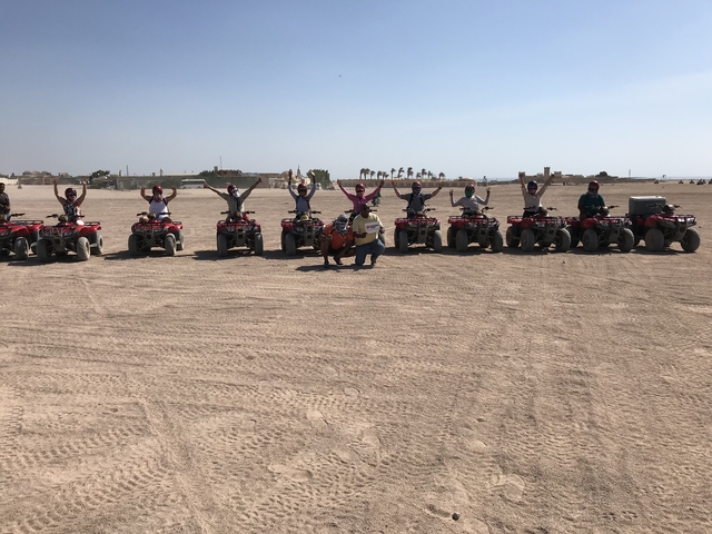       People on quad bikes in a desert landscape, raising their hands.
  