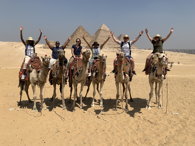       Group riding camels in front of the pyramids.
  