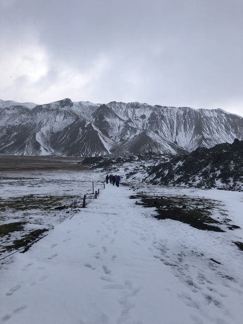 Group of people hiking on a snowy path in a mountainous area.