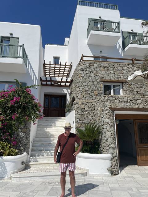 Man posing in front of a white stone building with a bougainvillaea plant.