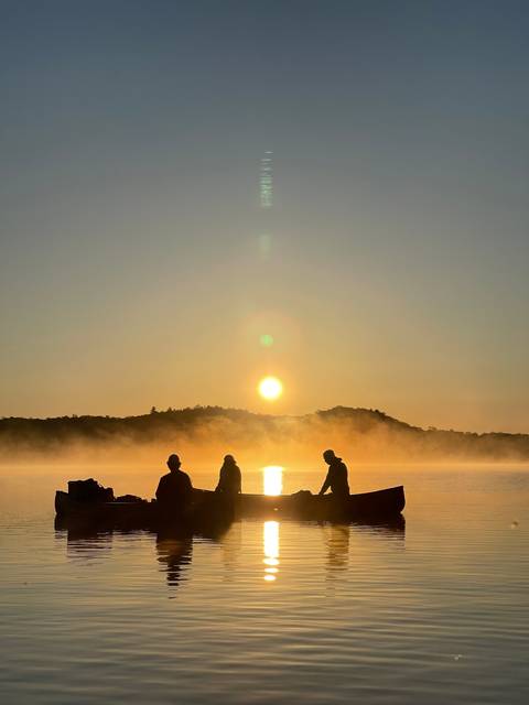 People in canoes on a lake during sunrise.