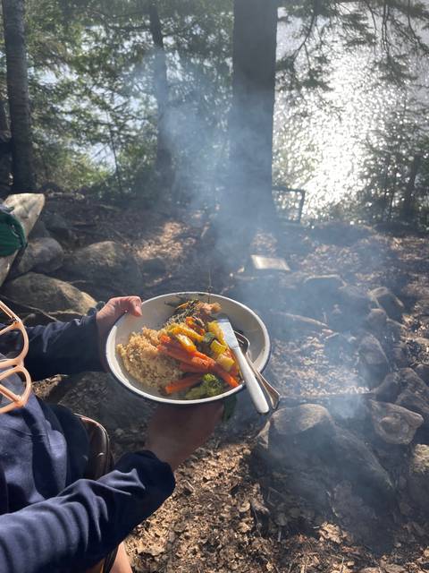       Plate of food held by a person in a forest setting.
  
