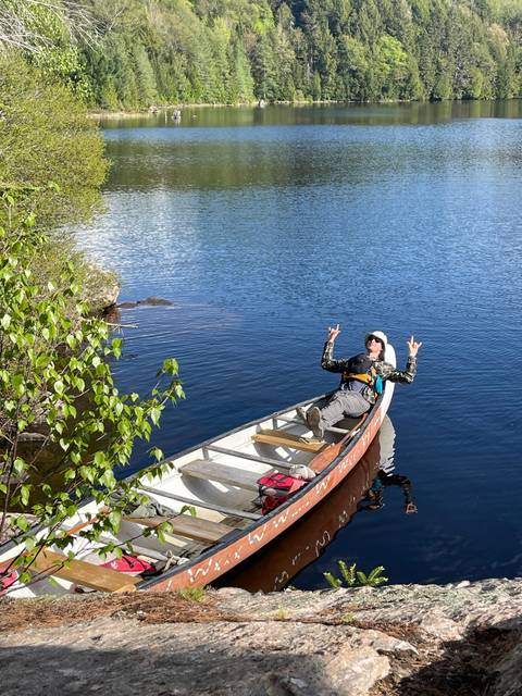 Person sitting in a canoe on a lake surrounded by trees.