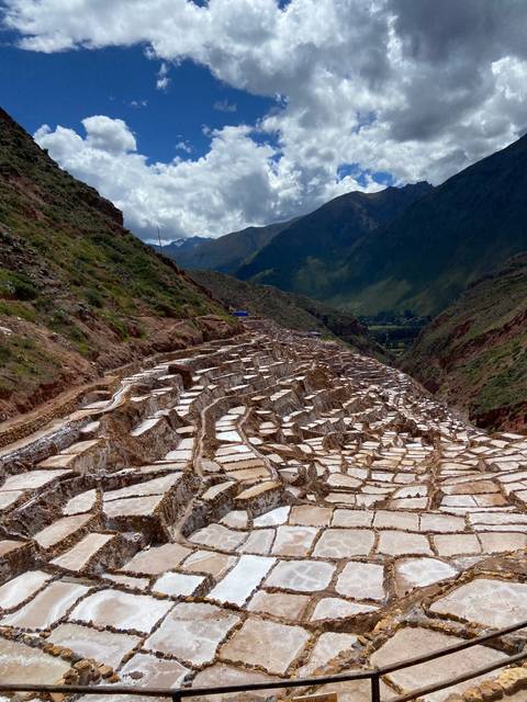 Salt terraces against a mountain backdrop with a blue sky.