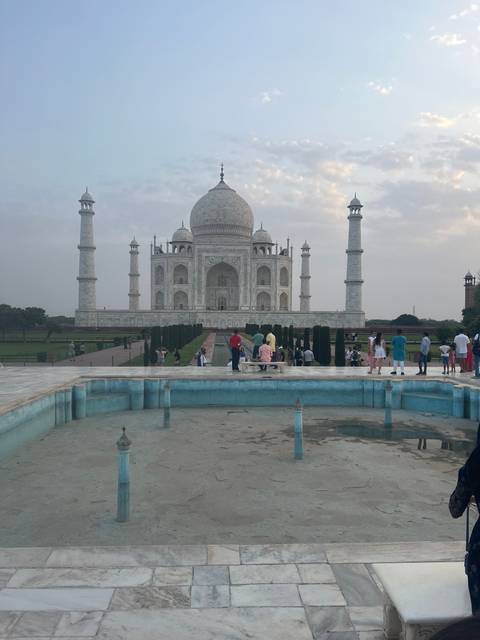       Taj Mahal with people in foreground and cloudy sky.
  