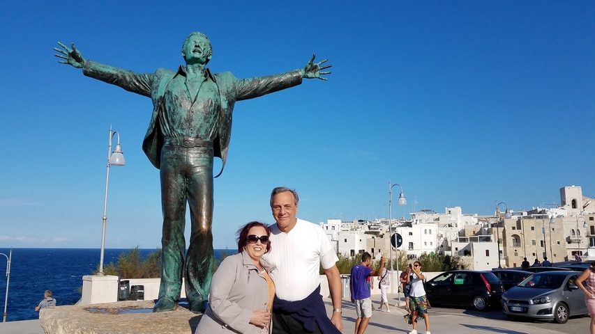 Couple posing with a large statue in a coastal town.