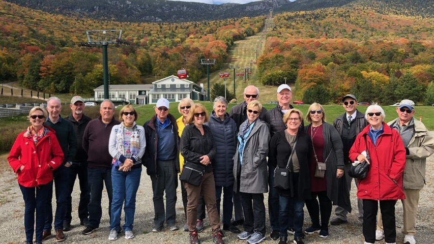 A group of people posing in front of a scenic mountain landscape in autumn.