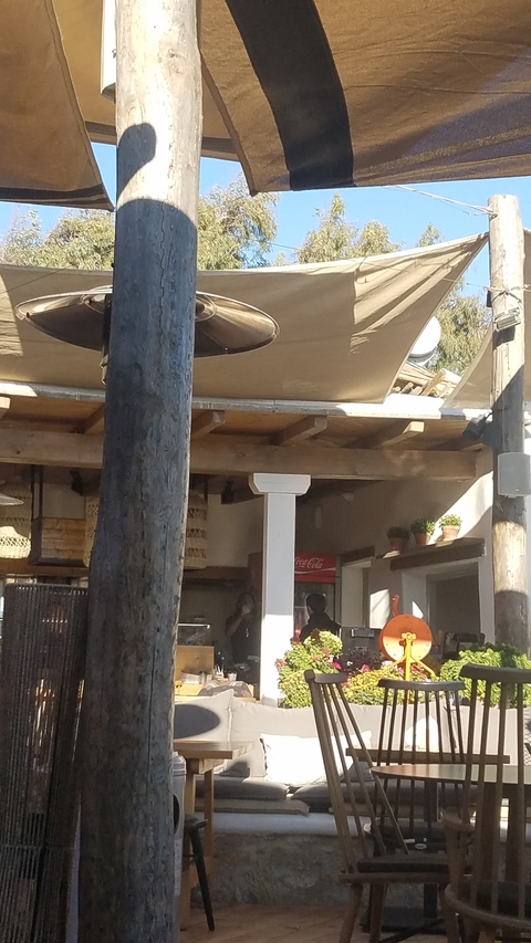       Outdoor cafe setting with wooden beams and a Coca-Cola fridge.
  