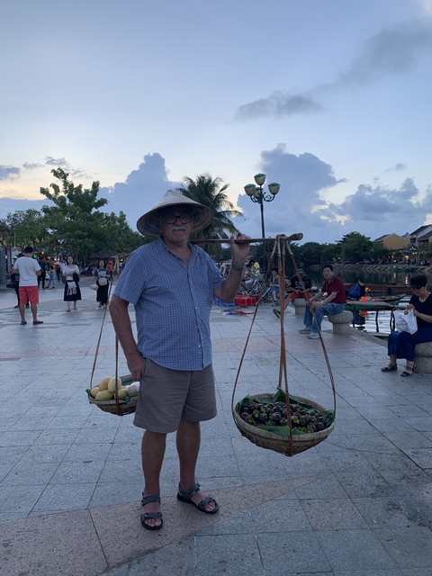 Man carrying baskets in a market area with people in background.