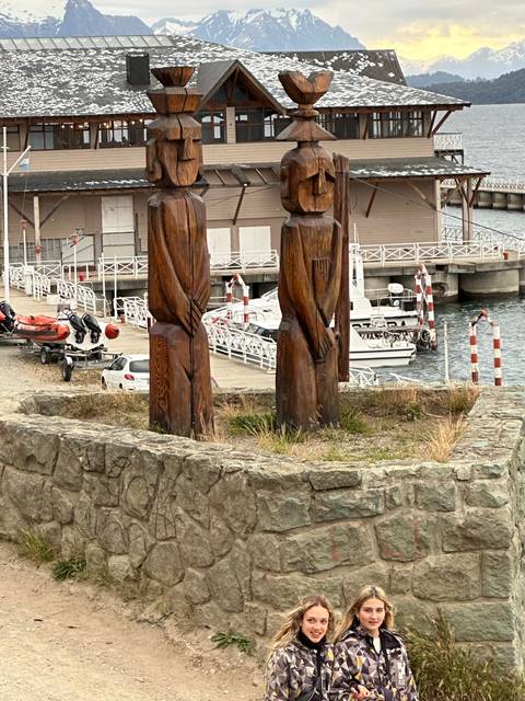       Two people posing near wooden statues by a waterfront.
  