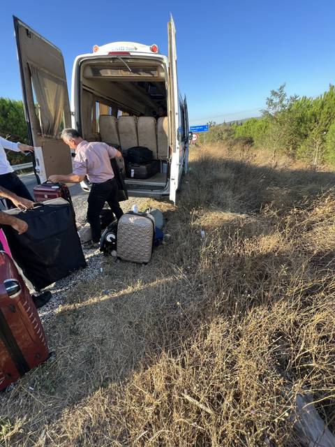       A traveler with luggage next to a bus on a rural road.
  