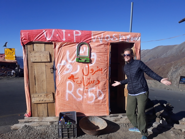 A woman posing playfully beside a small roadside structure.