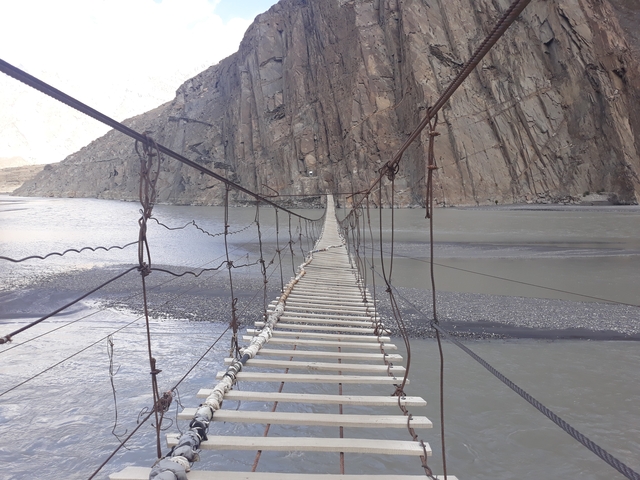 A suspension bridge over a river with rocky mountains in the background.