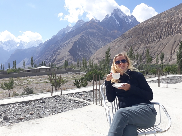       A woman enjoying a cup of tea with mountainous landscape in the background.
  
