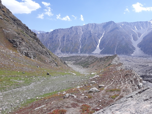       A valley with rocky mountains and patches of greenery.
  
