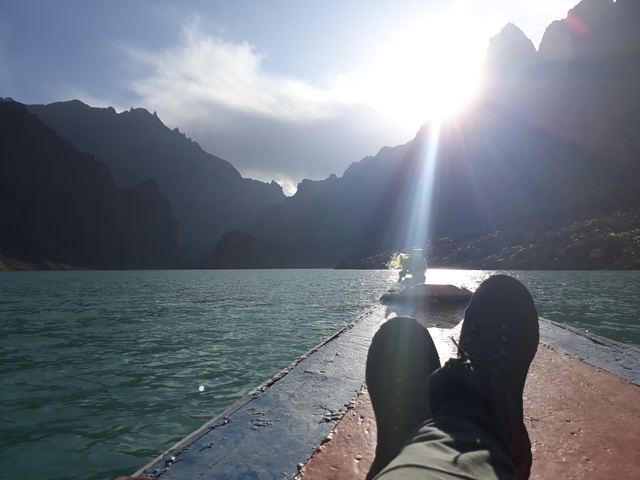       A serene view from a boat on a lake surrounded by mountains with the sun setting.
  