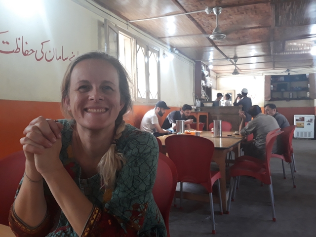       A smiling woman in a local restaurant with people in the background.
  