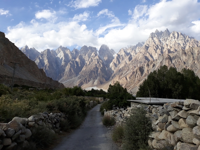 A scenic village pathway with rugged mountains in the background.
