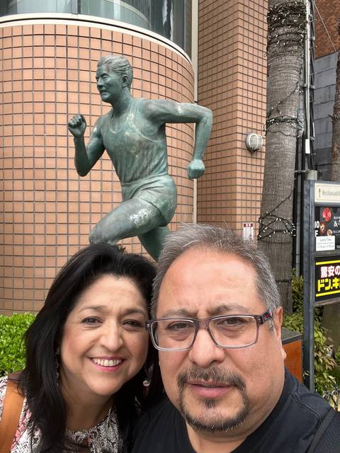       Two people taking a selfie with a bronze runner statue in the background.
  