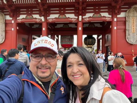      Two people in front of a red Buddhist temple.
  