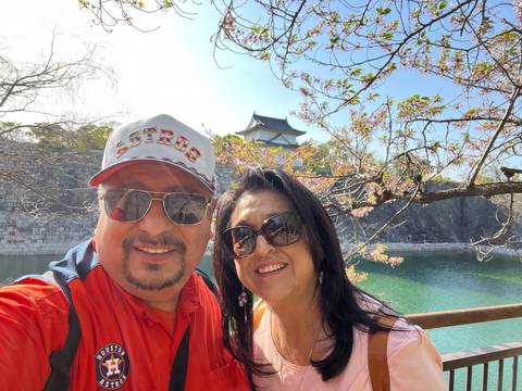       Two people taking a selfie in front of a lake and cherry blossoms.
  